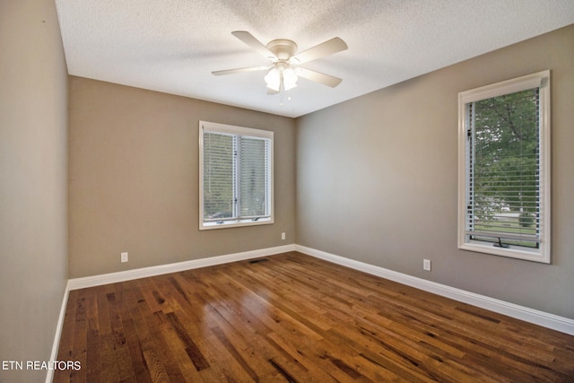 spare room with a textured ceiling, a healthy amount of sunlight, ceiling fan, and dark hardwood / wood-style flooring