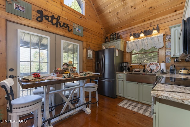 kitchen featuring light stone countertops, stainless steel fridge with ice dispenser, sink, and wooden walls