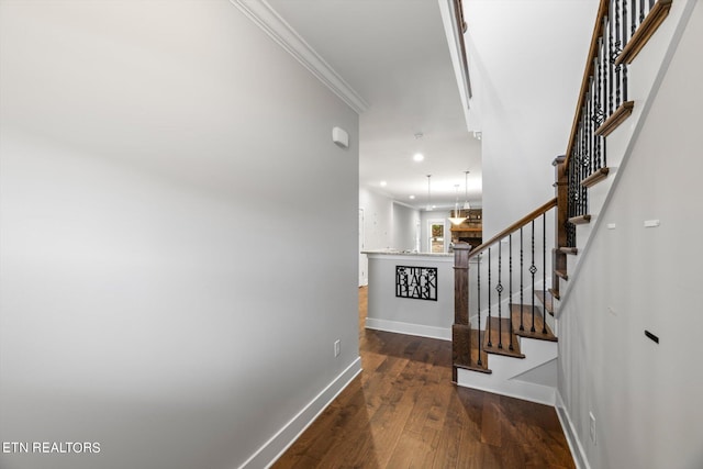 staircase featuring hardwood / wood-style flooring, crown molding, and an inviting chandelier