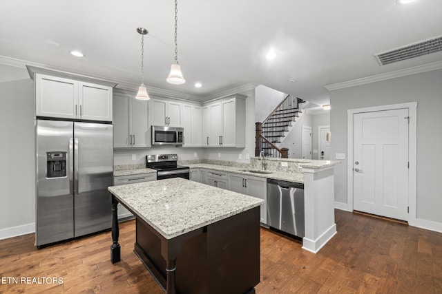 kitchen featuring dark wood-type flooring, light stone counters, stainless steel appliances, hanging light fixtures, and a center island