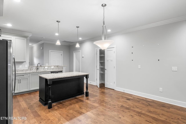 kitchen featuring light stone counters, stainless steel fridge, decorative light fixtures, a center island, and hardwood / wood-style floors