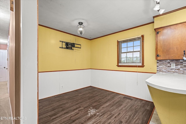 unfurnished dining area with a textured ceiling, wood-type flooring, ornamental molding, and wood walls