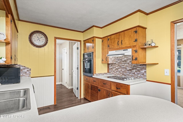 kitchen featuring tasteful backsplash, black appliances, dark wood-type flooring, crown molding, and sink