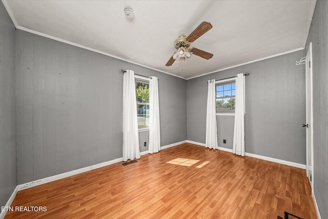 empty room with a wealth of natural light, crown molding, light hardwood / wood-style floors, and ceiling fan