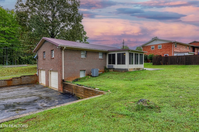 back house at dusk featuring a yard, a garage, a sunroom, and central AC unit