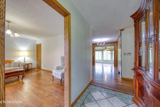 hallway featuring a notable chandelier, a textured ceiling, and light wood-type flooring