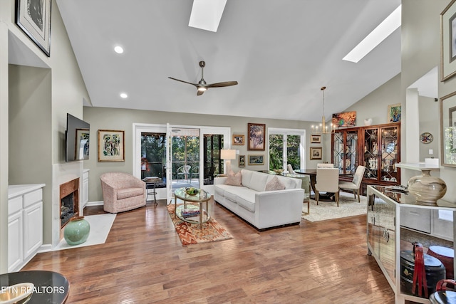 living room with hardwood / wood-style flooring, ceiling fan with notable chandelier, a skylight, and high vaulted ceiling