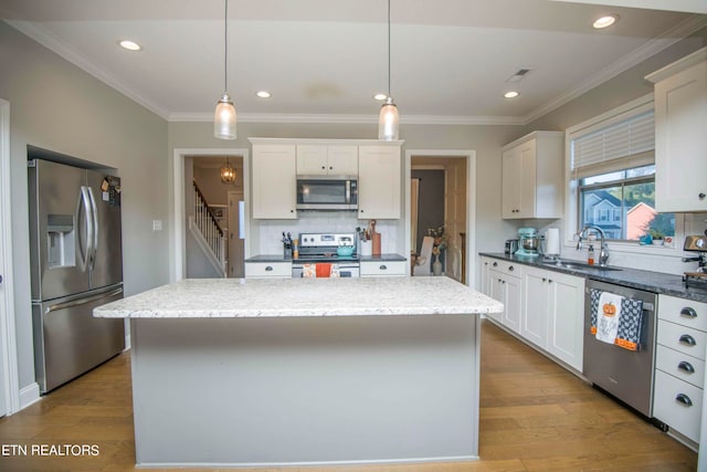 kitchen with decorative light fixtures, a center island, stainless steel appliances, and light hardwood / wood-style flooring