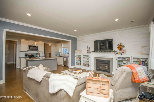 living room featuring ornamental molding, a tiled fireplace, dark wood-type flooring, and sink