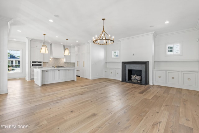 unfurnished living room featuring light wood-type flooring, crown molding, and a chandelier