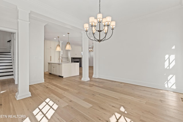 unfurnished living room featuring sink, light hardwood / wood-style flooring, decorative columns, a chandelier, and ornamental molding