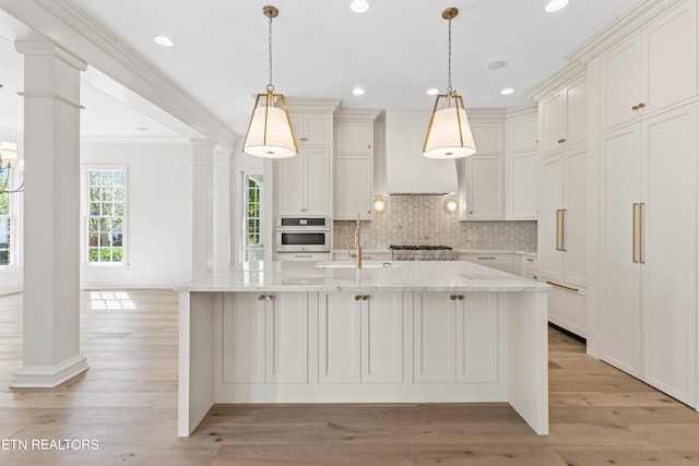 kitchen featuring pendant lighting, a center island with sink, oven, light stone countertops, and custom range hood