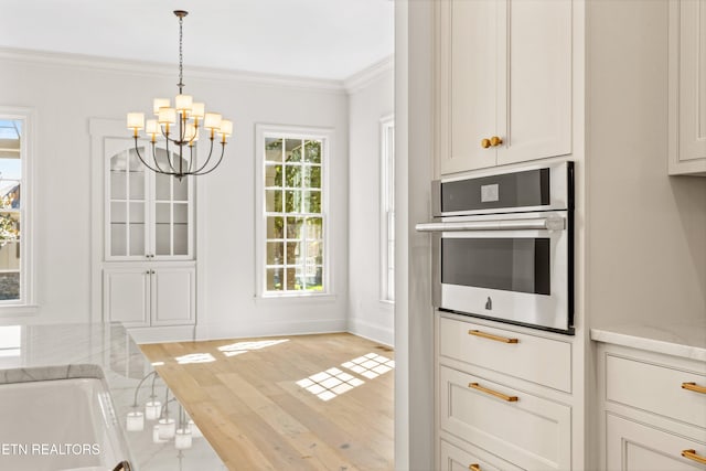 kitchen featuring light stone counters, crown molding, an inviting chandelier, light hardwood / wood-style flooring, and oven