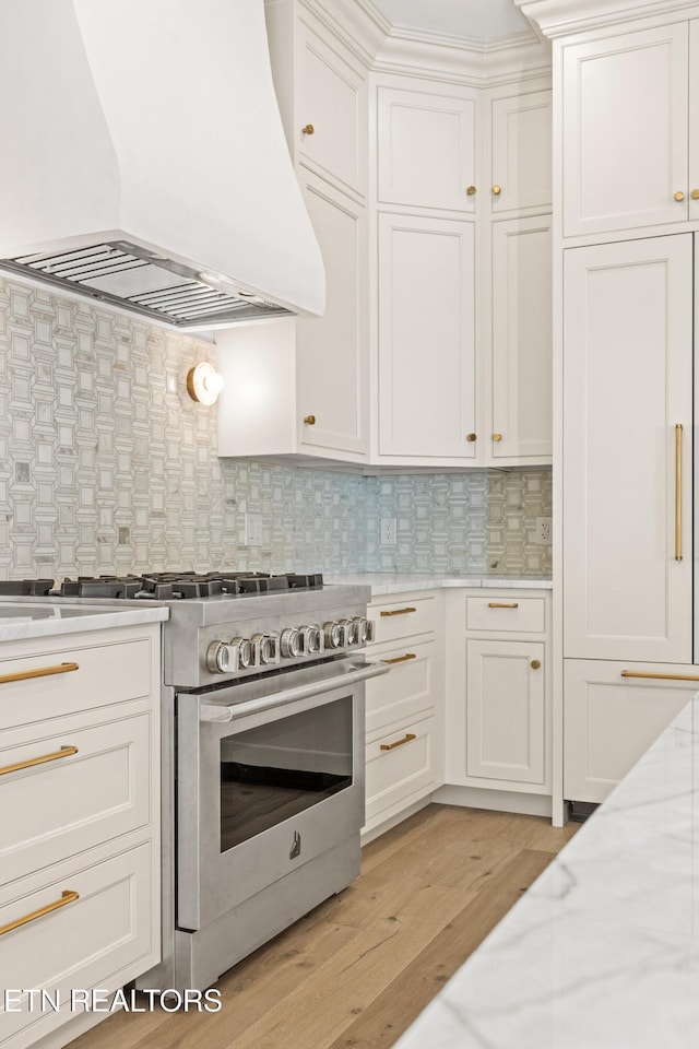 kitchen featuring light wood-type flooring, premium range hood, tasteful backsplash, white cabinets, and stainless steel stove