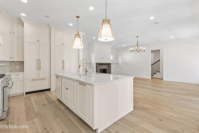 kitchen featuring light stone countertops, sink, decorative light fixtures, light hardwood / wood-style flooring, and an island with sink