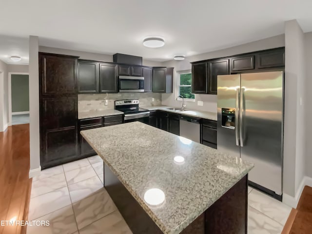 kitchen with sink, a kitchen island, backsplash, stainless steel appliances, and light stone countertops