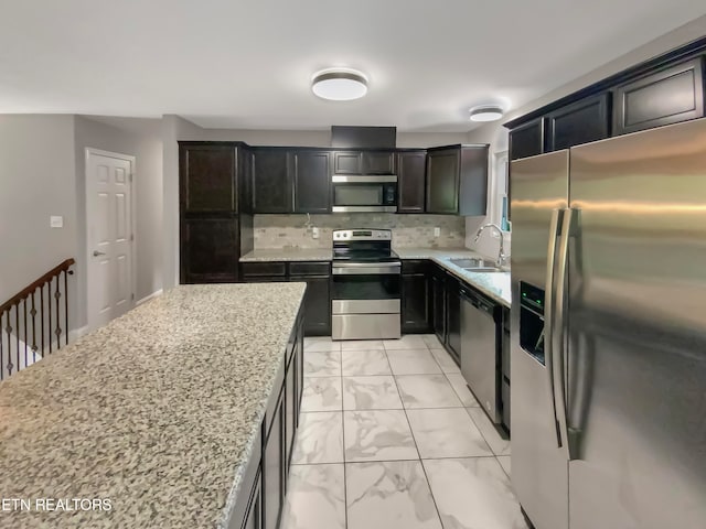 kitchen with appliances with stainless steel finishes, light stone countertops, sink, and tasteful backsplash