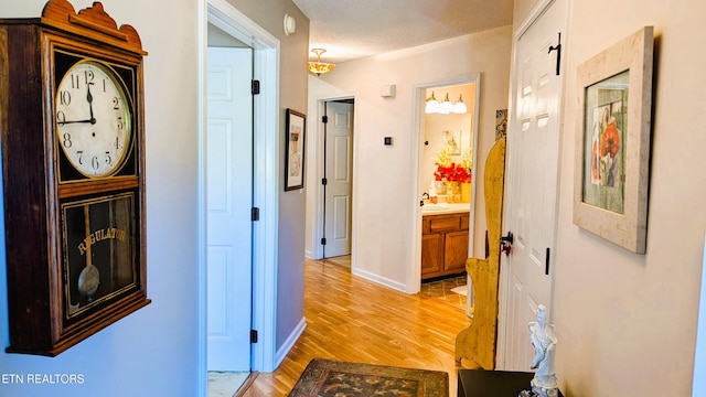 corridor with light wood-style flooring, baseboards, and a sink