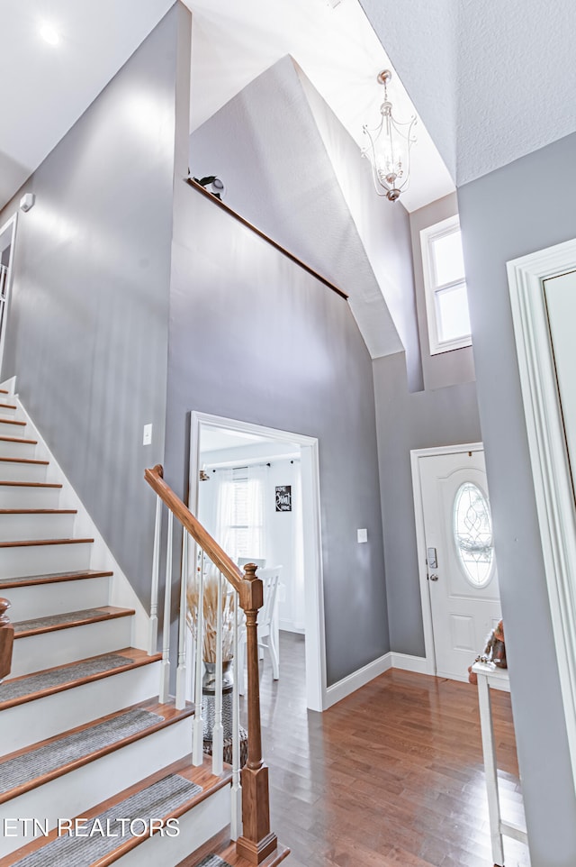 foyer entrance with a towering ceiling, hardwood / wood-style floors, and an inviting chandelier