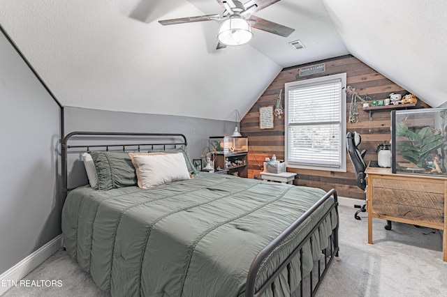 bedroom featuring ceiling fan, lofted ceiling, a textured ceiling, wooden walls, and light colored carpet