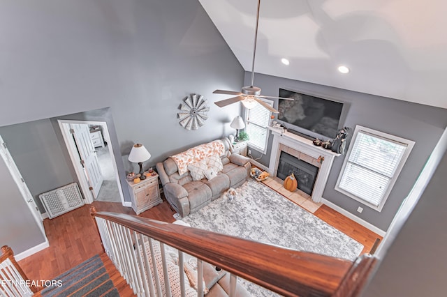 living room featuring ceiling fan, high vaulted ceiling, hardwood / wood-style floors, and a tiled fireplace