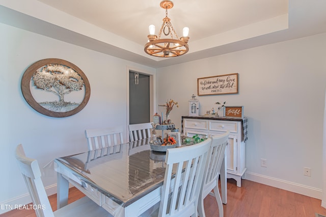 dining area with a notable chandelier, a raised ceiling, and light hardwood / wood-style flooring