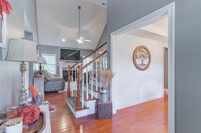 staircase with a fireplace, high vaulted ceiling, hardwood / wood-style floors, and ceiling fan