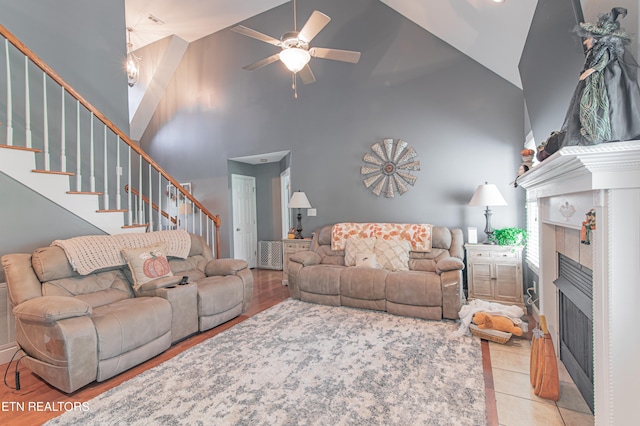 living room featuring high vaulted ceiling, ceiling fan, a tile fireplace, and light hardwood / wood-style flooring