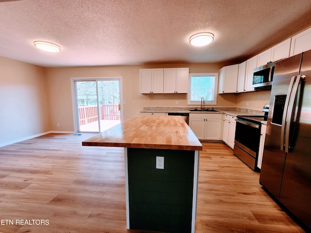 kitchen with appliances with stainless steel finishes, light hardwood / wood-style flooring, a center island, and white cabinets