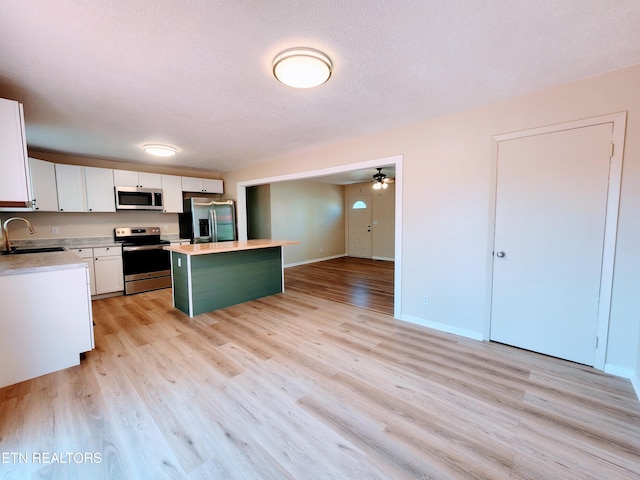 kitchen featuring a center island, stainless steel appliances, white cabinets, sink, and light hardwood / wood-style flooring