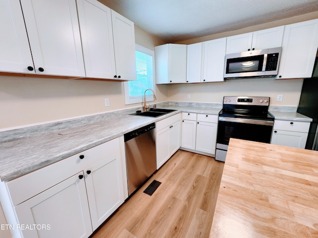 kitchen featuring appliances with stainless steel finishes, light wood-type flooring, sink, and white cabinetry