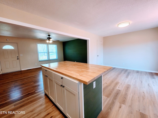 kitchen featuring light hardwood / wood-style flooring, wood counters, white cabinets, a center island, and a textured ceiling