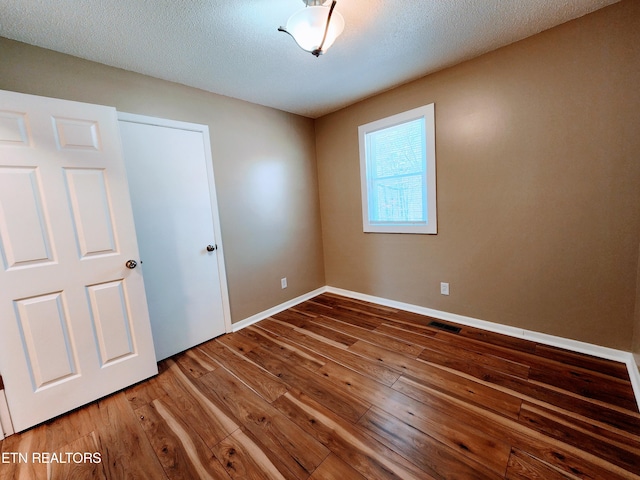 unfurnished room with wood-type flooring and a textured ceiling