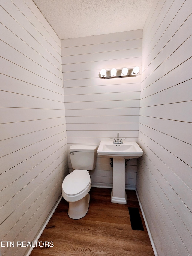 bathroom with toilet, wooden walls, hardwood / wood-style floors, and a textured ceiling