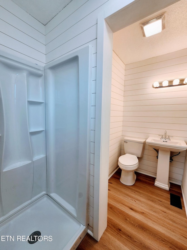 bathroom featuring a shower, hardwood / wood-style floors, wooden walls, and toilet