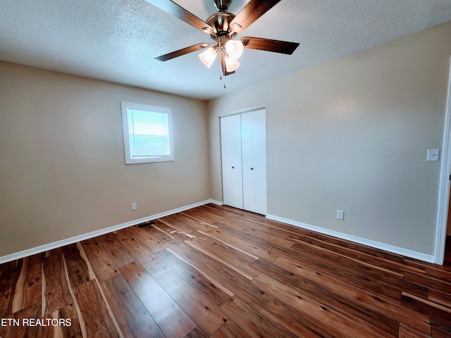 unfurnished bedroom featuring ceiling fan, a textured ceiling, a closet, and dark hardwood / wood-style flooring