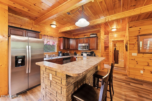 kitchen with pendant lighting, appliances with stainless steel finishes, wood walls, and light hardwood / wood-style flooring