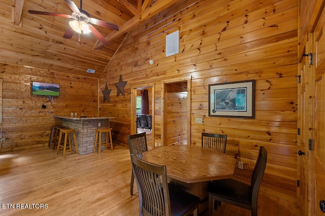 dining room featuring lofted ceiling with beams, light wood-type flooring, ceiling fan, wooden ceiling, and wooden walls