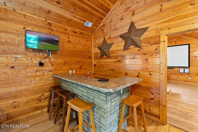 bar featuring lofted ceiling, wood walls, wood ceiling, and light hardwood / wood-style floors