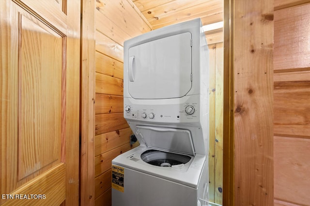 laundry area with wood walls and stacked washing maching and dryer