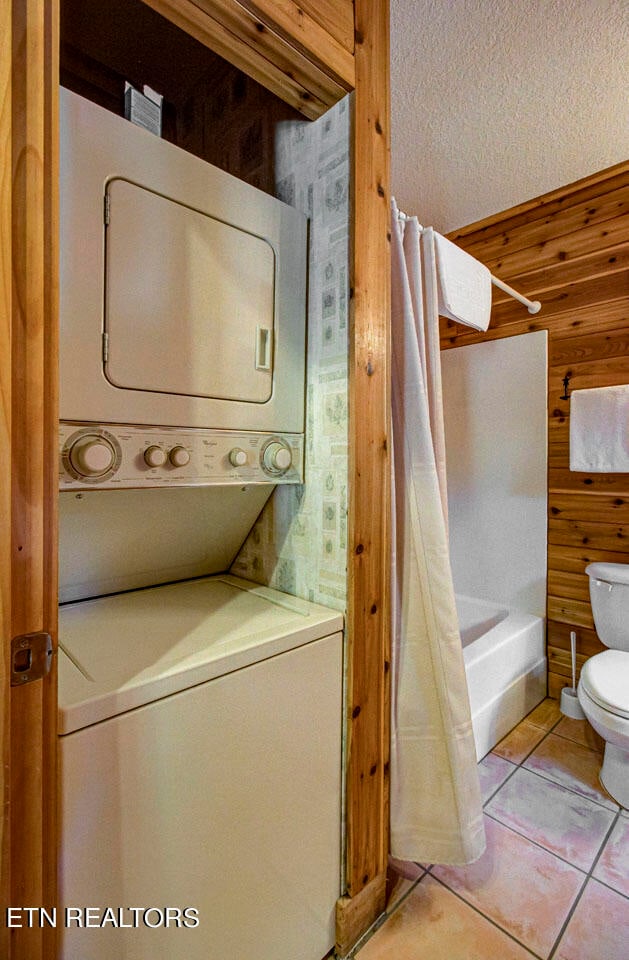 clothes washing area featuring wooden walls, light tile patterned floors, and stacked washing maching and dryer