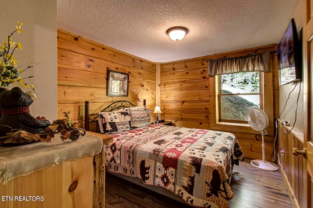 bedroom with a textured ceiling, dark hardwood / wood-style floors, and wood walls