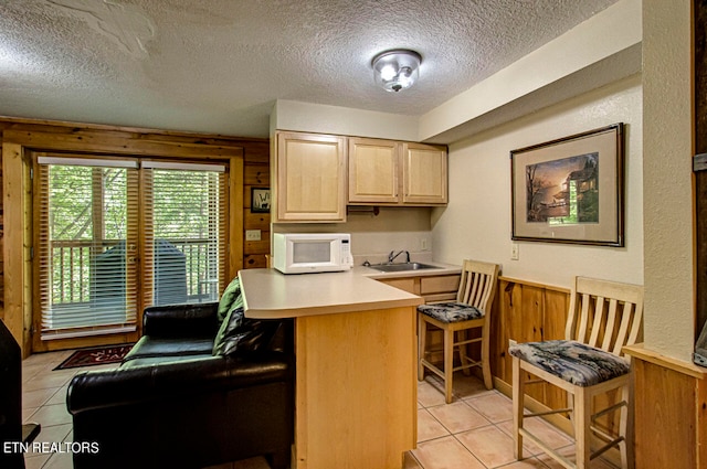 kitchen featuring kitchen peninsula, light brown cabinetry, wood walls, a kitchen breakfast bar, and a textured ceiling