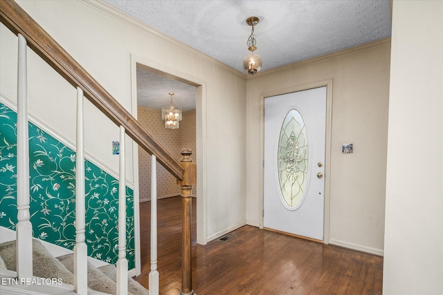 entrance foyer with dark wood-type flooring, a textured ceiling, an inviting chandelier, and crown molding