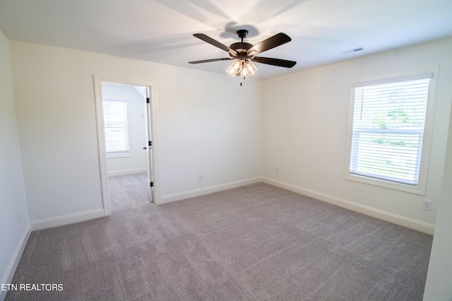 carpeted empty room with baseboards, a ceiling fan, and visible vents