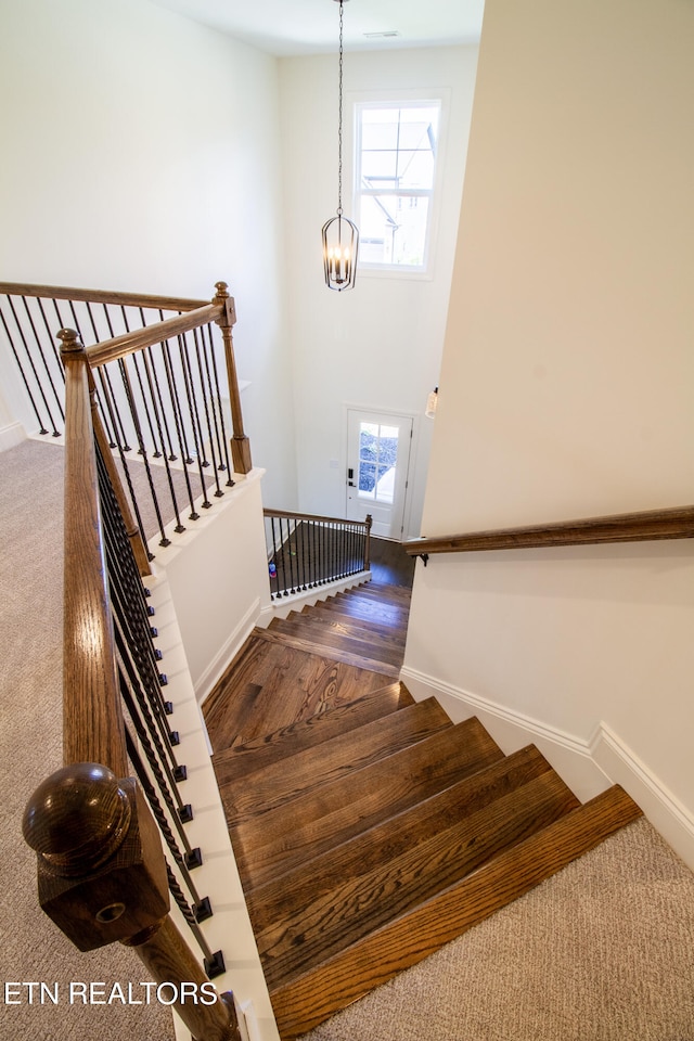 stairs with hardwood / wood-style floors, a wealth of natural light, and a chandelier