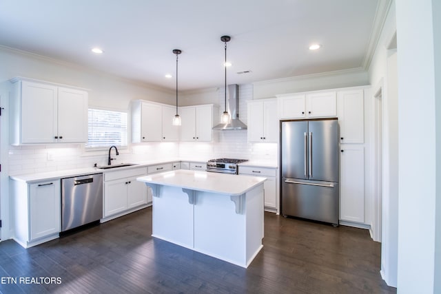 kitchen with crown molding, wall chimney range hood, white cabinets, a sink, and appliances with stainless steel finishes