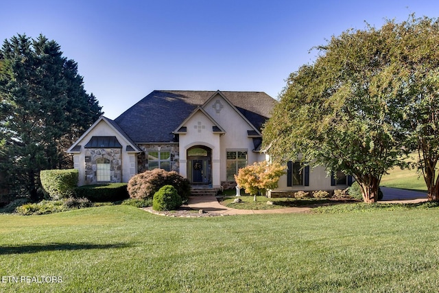 french country inspired facade featuring stucco siding, stone siding, roof with shingles, and a front yard