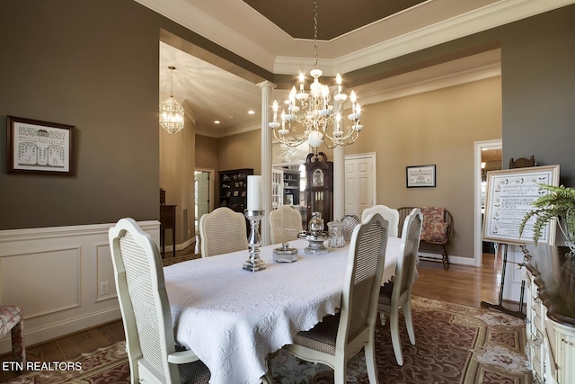 dining area with wood finished floors, a wainscoted wall, an inviting chandelier, ornamental molding, and a decorative wall