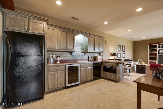 kitchen with visible vents, beverage cooler, a peninsula, black appliances, and a sink